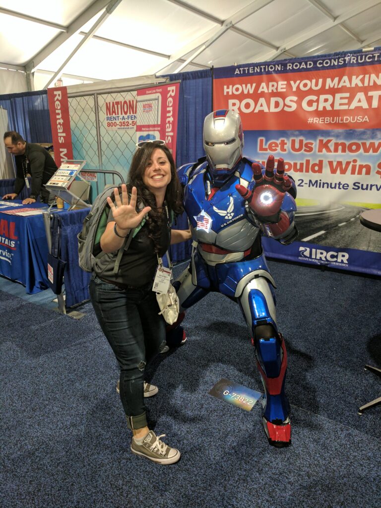 A woman poses playfully with a lifelike robotic figure resembling an armored superhero