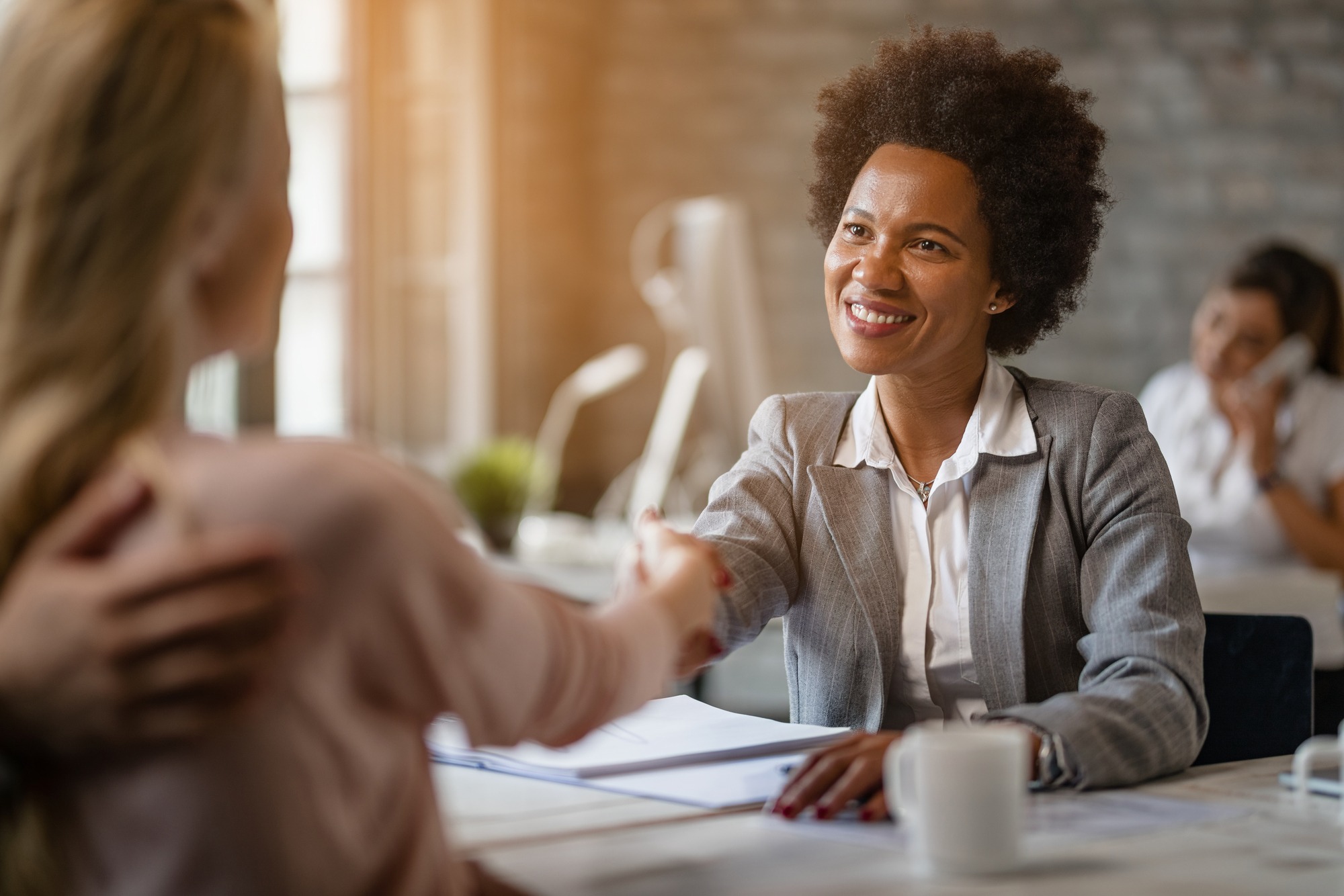 Happy African American bank manager shaking hands with her clients after the meeting